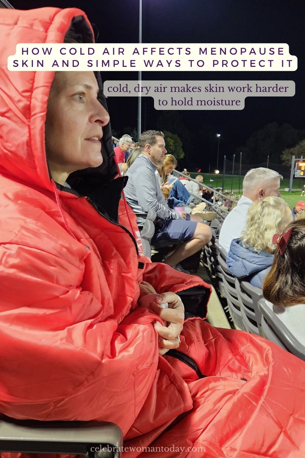 Woman bundled in a warm, hooded stadium sak at a cold outdoor evening sports event, smiling and ready to watch the game.