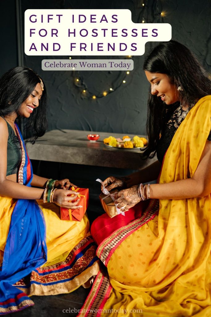 Two women in colorful saris sitting together and tying ribbons on small gifts under string lights