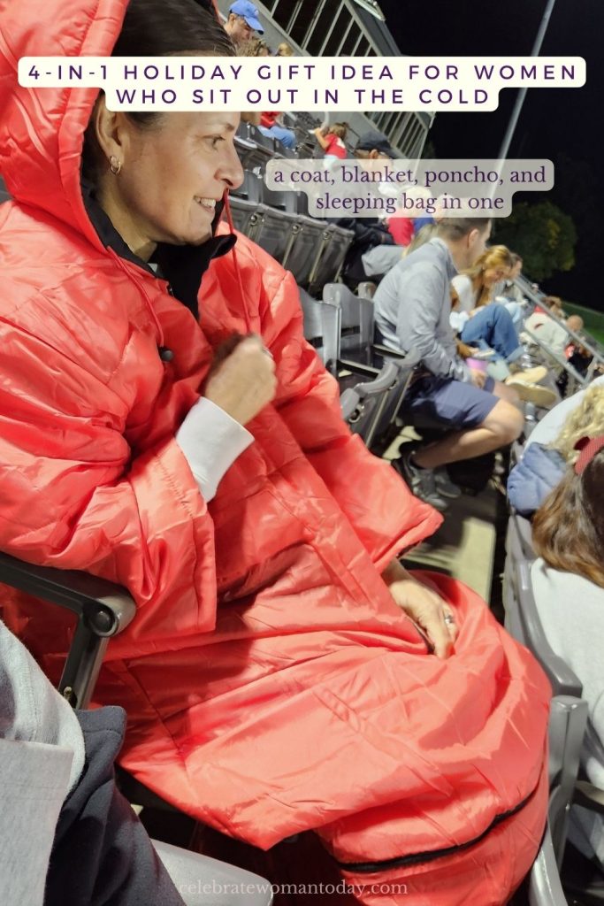 Woman in a red hooded Ultimate Stadium Sak holding open the lower bottom section, beside a checklist reading coat, blanket, poncho, and sleeping bag on a dark, smoky background.