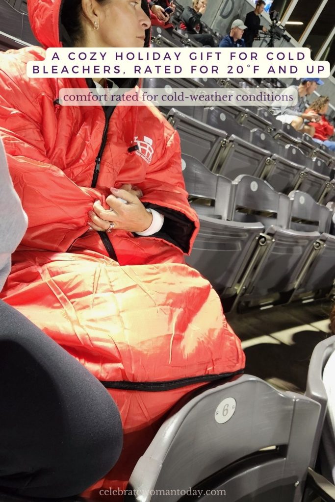 Woman in a navy blue Ultimate Stadium Sak sitting on snowy stadium bleachers, with text reading Comfort Rated for 20 degrees plus, cold-weather conditions starting at 20°F and up.