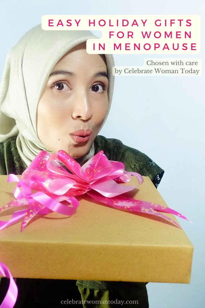 Woman in a beige headscarf holding a large kraft gift box with a bright pink bow and a playful expression